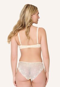 Komplet koronkowy z biustonoszem i majtkami w kremowym kolorze, z kwiatowym wzorem koronki, regulowanymi ramiączkami i przezroczystym wykończeniem. Gładka tkanina z miękkimi krawędziami.