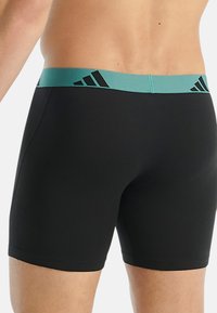 Zwarte aansluitende boxershorts met een turquoise elastische tailleband en zwarte logo-accenten. Glad textuur en knie-lange ontwerp.