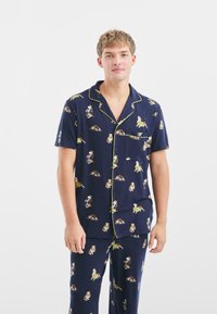 Pijamas azul marino con un patrón de perros, hechos de un tejido suave, con mangas cortas, un bolsillo y ribetes amarillos en contraste a lo largo de los bordes.