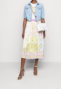 Jeansowa kurtka, kwiecista pastelowa sukienka midi z plisami, złote sandały na szpilkach oraz biała torebka z ćwiekami, z misternymi wzorami i detalami.