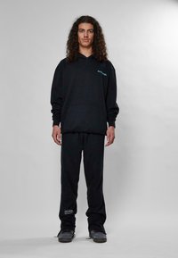 Felpa nera con tasca a marsupio e testo turchese. Abbinata a pantaloni della tuta neri, con una vestibilità aderente e un branding discreto.