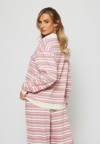 Cienki sweter w miękkim materiale w różowe, kremowe i niebieskie poziome paski. Posiada kołnierzyk oraz ściągacze przy dolnej krawędzi i rękawach.