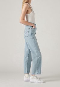 Vaqueros de mezclilla azul de talle alto con un ajuste relajado, que cuentan con dos bolsillos laterales, bolsillos traseros y un acabado deslavado. Combinados con zapatillas blancas.