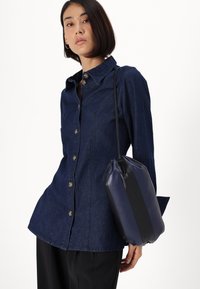 Tummansinisestä denimistä valmistettu kauluspaita, jossa nappisuljenta, kaulus ja pitkät hihat; yhdistettynä laivastonsiniseen ja mustaan nahkalaukkuun, joka näyttää sileältä.