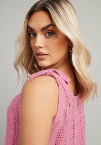 Rosa stickad topp med spetsmönster, med en knytdetalj på axeln och en avslappnad passform, som visar ett strukturerat och lätt material.