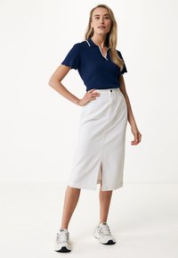 Camisa polo navy con detalle de cuello blanco, combinada con una falda blanca hasta la rodilla con una abertura frontal, llevada con zapatillas blancas.