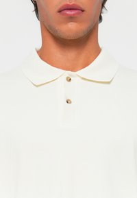 Hvit stripete polo skjorte med en strukturert krave, med to knapper i kontrastfarger ved halsen for lukking.