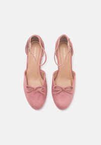 Paire de ballerines en daim rose avec brides à la cheville et petits nœuds sur les orteils, vues de dessus sur fond blanc.
