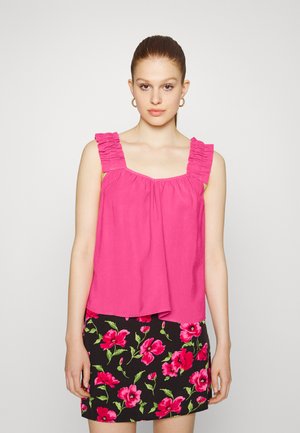 Camisola sem mangas de cor rosa brilhante com alças franzidas, apresentando um corte solto. Combinada com uma saia preta adornada com grandes padrões florais rosas.