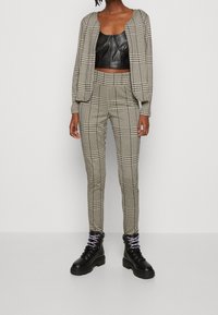 Tenue en tissu à carreaux comprenant un haut en cuir noir court, un pantalon à carreaux assorti et des bottes de combat noires épaisses avec des lacets violets.