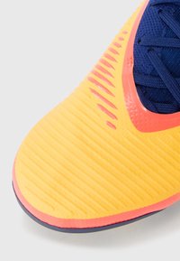 Bright yellow athletic shoe toe with textured ridges, featuring a pink accent and navy fabric laces. Round shape with a smooth finish.