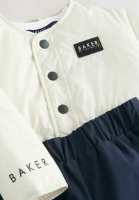 Hellbeige Steppjacke mit navyfarbenem elastischem Bund, drei schwarzen Knöpfen und einem schwarzen Etikett mit weißer Aufschrift "BAKER".