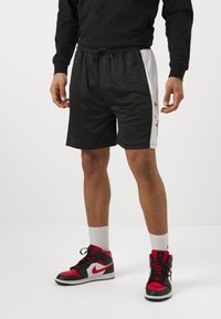 Svarte idrettsshorts med hvite og røde sidepaneler, mesh-struktur, elastisk midjebånd og snor. Kombinert med røde og svarte høye sneakers.