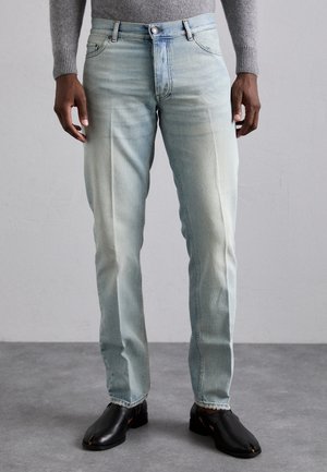 Light blue denim jeans with a slim fit. Features a button closure and four pockets. Paired with black leather shoes.