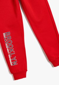 Czerwone dresy wykonane z miękkiej bawełny. Posiadają elastyczne mankiety i nadrukowany tekst "BROOKLYN" w kontrastowych kolorach na lewym nogawce.