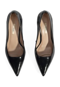 Zwarte gepatineerde leren hoge hakken met een spitse neus, met een gladde textuur en een beige interieurvoering, gelabeld "DESA."