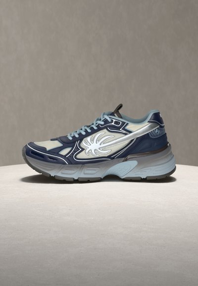 Μπλε και γκρι αθλητικό παπούτσι με λευκό σχέδιο φλόγας στο πλάι, γαλάζια κορδόνια και χοντρή υφή στη σόλα, σε ουδέτερη επιφάνεια και φόντο.