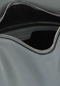 Interno di una borsa in pelle grigia con fodera in tessuto nero, dotato di una tasca con cerniera e una cerniera grigia con accessori in argento.