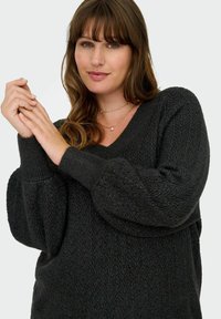 Tmavošedý pletený sveter s výstrihom do V, textúrovaným rybím vzorom a prehnanými rukávmi. Materiál sa javí ako mäkký a útulný.