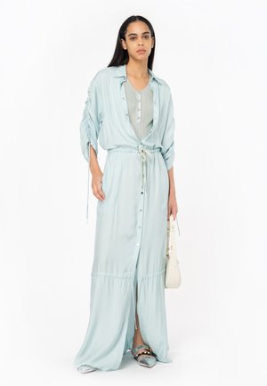 Robe maxi bleu clair avec fermeture à boutons et taille à cordon; présente des manches longues et des poches latérales; stylée avec des sandales argentées.