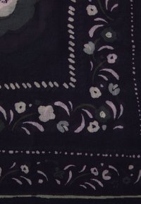 Blomstermønstret tørklæde med en mørk baggrund. Har lilla og hvide blomster, intrikate scroll-detaljer og en kantet kant.