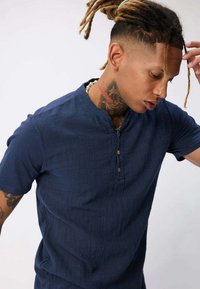 Chemise bleu marine à manches courtes en tissu texturé, avec un col mao et trois boutons au niveau de l'encolure.