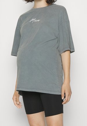 Grijze oversized t-shirt met korte mouwen, voorzien van witte borduursel "Mama". Gecombineerd met zwarte shorts, die een relaxte pasvorm en zachte textuur laten zien.