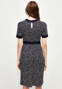 Vestido de manga corta y largo hasta la rodilla en color marino con un patrón de rejilla blanca texturizada. Presenta una cintura ajustada y un detalle de escote en forma de llave en la parte posterior.
