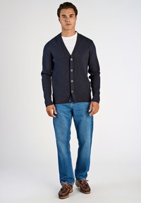 Marinblå ribbad cardigan med V-ringning, med knappar fram, i kombination med ljusblå raka jeans och bruna skor.