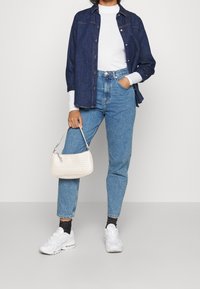 Džínová košile, bílý dlouhý rukáv, modré džíny s vysokým pasem, bílé tenisky a malá pletená bílá kabelka; ležérní outfit s různorodými texturami.