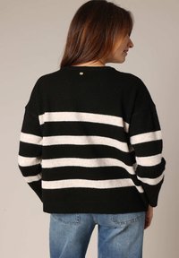 Pull rayé noir et blanc, fabriqué en tissu doux, avec une coupe décontractée, un col rond et un petit logo au dos.