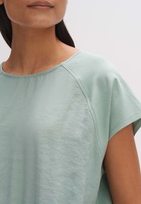 Jasnozielony, krótko rękawowy top wykonany z miękkiego materiału. Posiada okrągły dekolt oraz rękawy raglanowe, co zapewnia luźny krój i gładką fakturę.