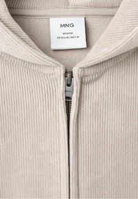 Giacca in corduroy beige con zip, dotata di colletto alto, featuring zip in metallo e etichetta che indica la taglia EU M/MEX M. Texture morbida.