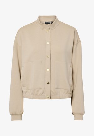 Bēši krāsots garu piedurkņu žakete ar stāvošu apkakli, zelta klipšiem priekšpusē, divām lielām priekšējām kabatām un elastīgu jostu un aprocēm.