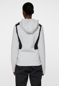 Huvtröja i ljusgrått med svarta accenter. Har strukturerad tyg och en figurnära design med unika axelpane-linjer.