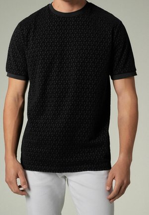 Camiseta negra de manga corta con un patrón geométrico texturizado, cuello y puños acanalados, combinada con pantalones blancos.