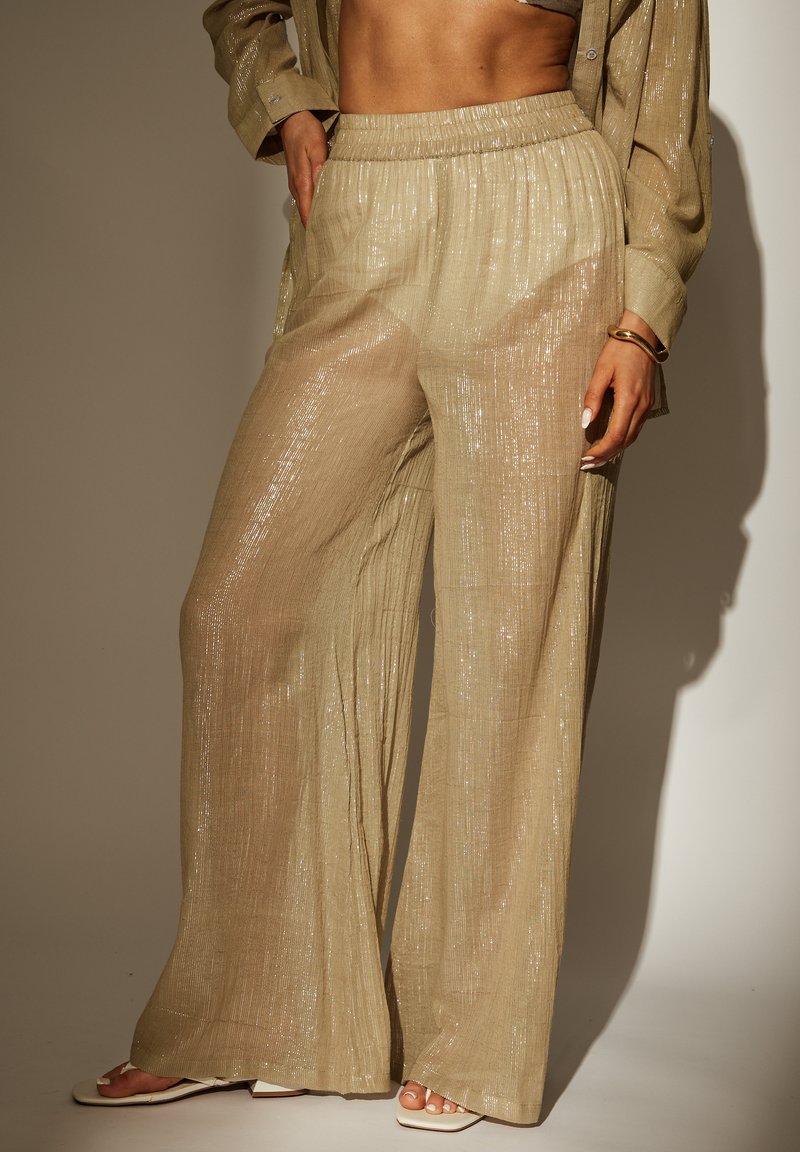Transparante beige wijde broek met een gestructureerde afwerking en subtiele glans, met een elastische tailleband en een vloeiende silhouet.