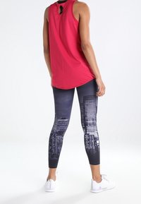 Top rosso senza maniche con dettaglio a chiave sul retro abbinato a leggings scuri con stampa di skyline cittadino in bianco e grigio. Scarpe da ginnastica bianche.
