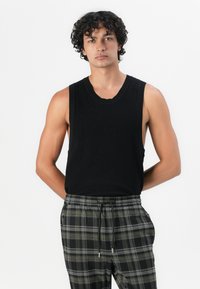 Schwarzes ärmelloses Tanktop in gerippter Textur, kombiniert mit grauen und schwarzen karriertem Hosen mit elastischem Bund. Einfaches Design, keine Verzierungen.