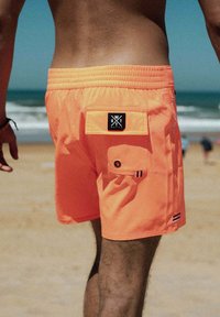 Heldere oranje zwembroek met een elastische tailleband, zijzak en merkpatch. Heeft subtiele gestreepte accenten langs de zoom.