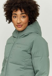 Padded jacket in muted green with a hood, featuring a zip closure and stitched panel design. Logo visible on the left chest area.