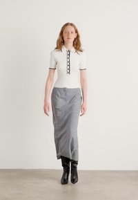 Witte geribde polo met korte mouwen en zwarte knopen, gecombineerd met een grijze lange kokerrok en zwarte kniehoge laarzen. Minimalistisch design, gladde textuur.