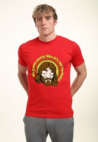 Camiseta de algodón roja con un gráfico de una cara con barba y ojos cerrados, rodeada de texto y un diseño de rayos de sol en amarillo y marrón.
