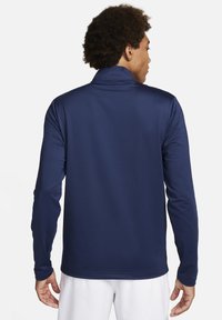 Camisola atlética de manga longa em azul-marinho, feita de um tecido suave com colarinho alto. Apresenta um padrão texturizado e um silhueta elegante.