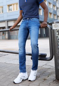 Přiléhavé světle modré džínsy z denimu s jemným vyblednutím, doplněné bílými teniskami s černými detaily a námořnicky modrým polo tričkem.