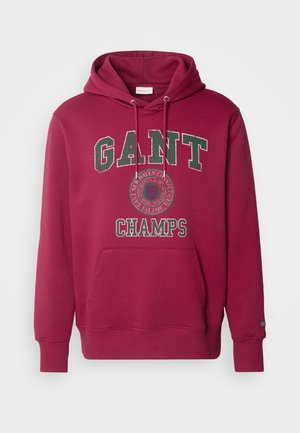 Burgundi GANT kapucnis felső, amely zsinóros kapucnival, elülső zsebbel és "GANT" valamint "CHAMPS" grafikával díszített. Pamut anyag, laza szabás.