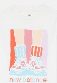 Bela srajca s pisanim grafičnim prikazom nog v črtastih nogavicah in supergah New Balance, z besedilom "new balance" spodaj v pastelnih barvah.