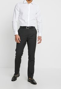 Camicia bianca con bottoni, pantaloni grigi slim-fit, cintura nera con fibbia argentata e mocassini neri. Tessuto liscio con una silhouette sartoriale.
