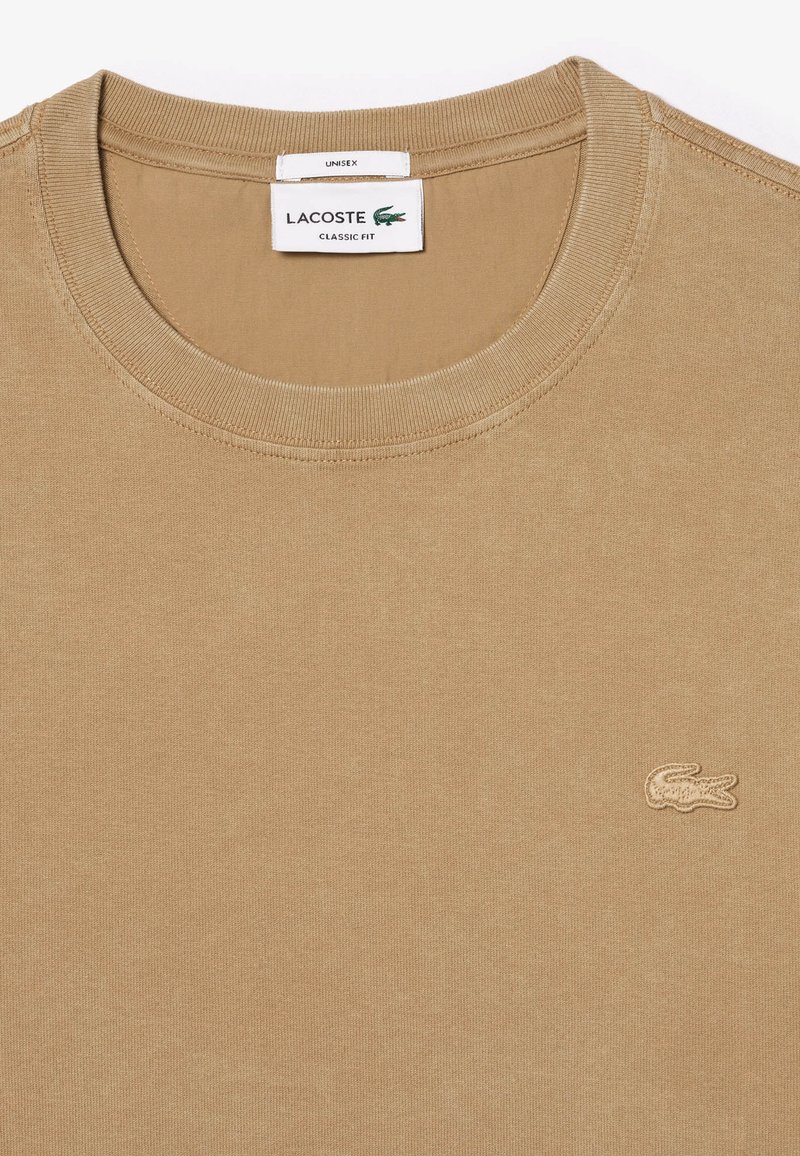 Beige Baumwoll-T-Shirt mit Rundhalsausschnitt und geripptem Kragen, mit einem kleinen, gestickten Logo auf der linken Brust. Klassisches Passform-Design.