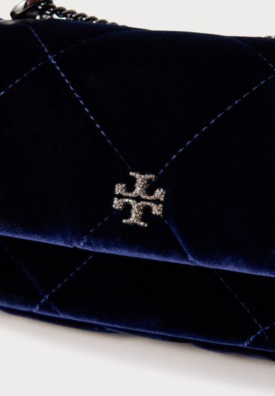 Carteira azul-marinho em veludo com design acolchoado, apresentando ferragens em tom prateado e um destaque de logótipo proeminente no centro.